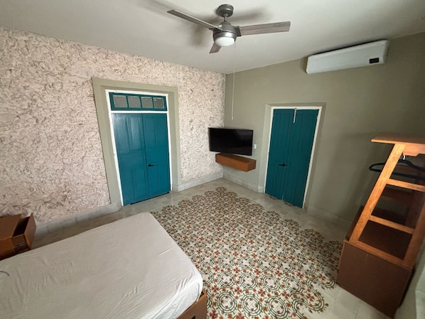 Un dormitorio con cama, ventilador de techo, televisor montado en la pared y dos puertas.