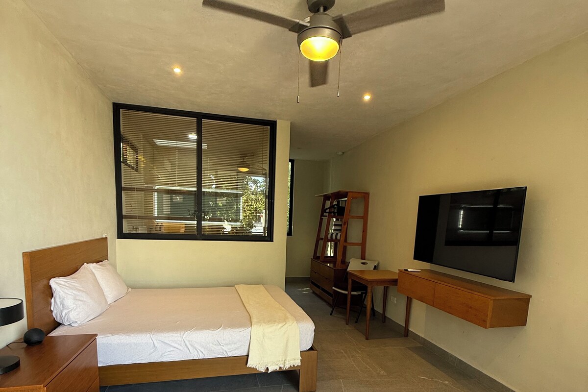 A hotel room with a bed, a desk, a chair, a television, and a ceiling fan.