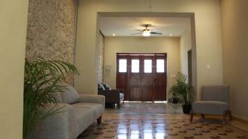 A spacious living area with a patterned floor, a ceiling fan, and a large wooden door.