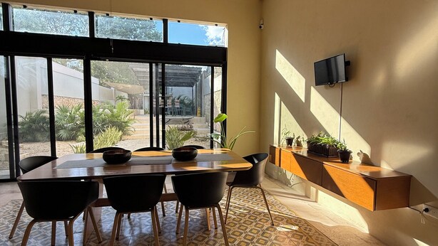 A dining area with a table, chairs, a ceiling fan, and a view through large windows. - Casa Xunan (Mérida)