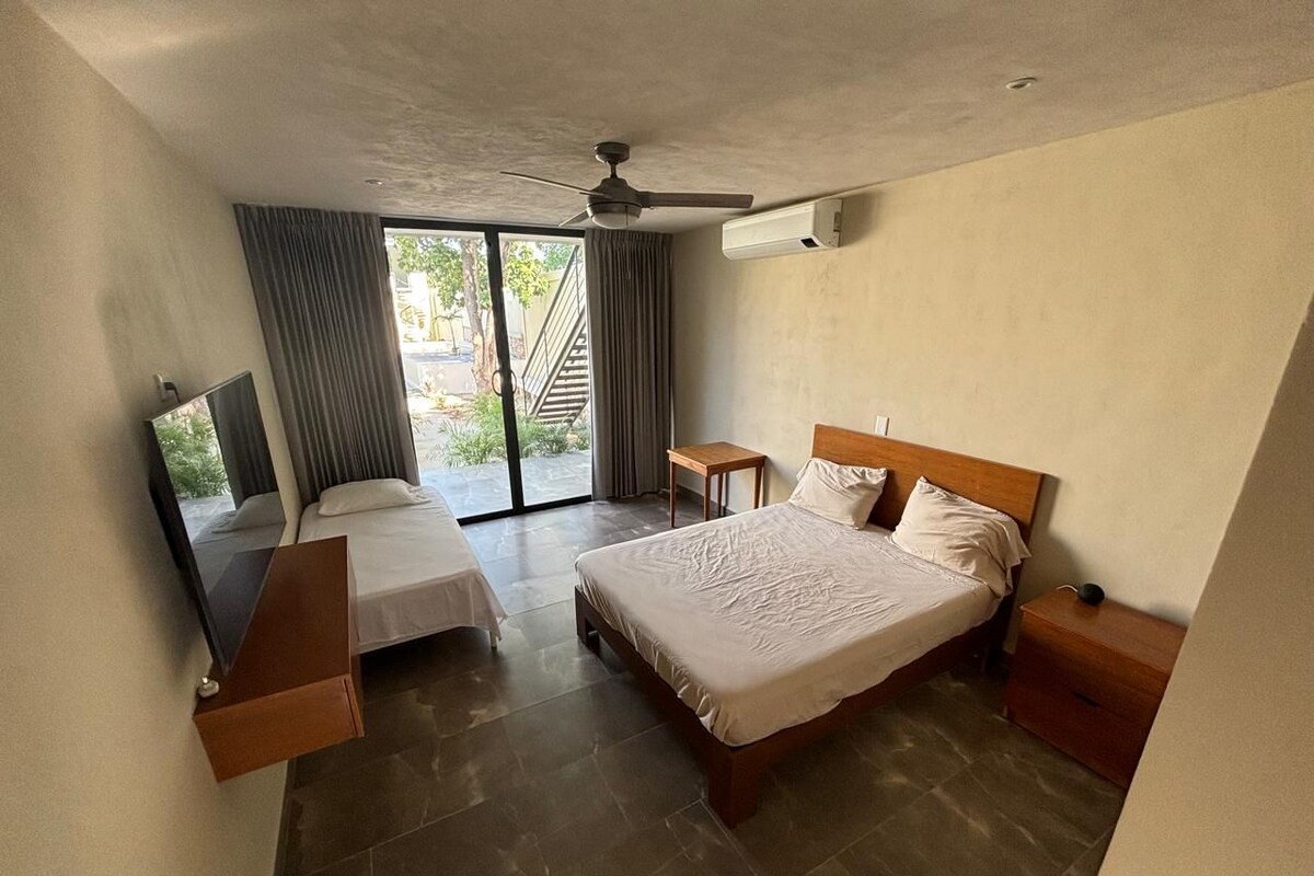 A hotel room with a bed, bedside tables, a TV, and a sliding glass door to the outside.