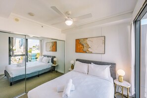 Ein Hotelzimmer mit einem großen Bett, einem Deckenventilator, Blick auf die Stadt und einem Bild an der Wand.