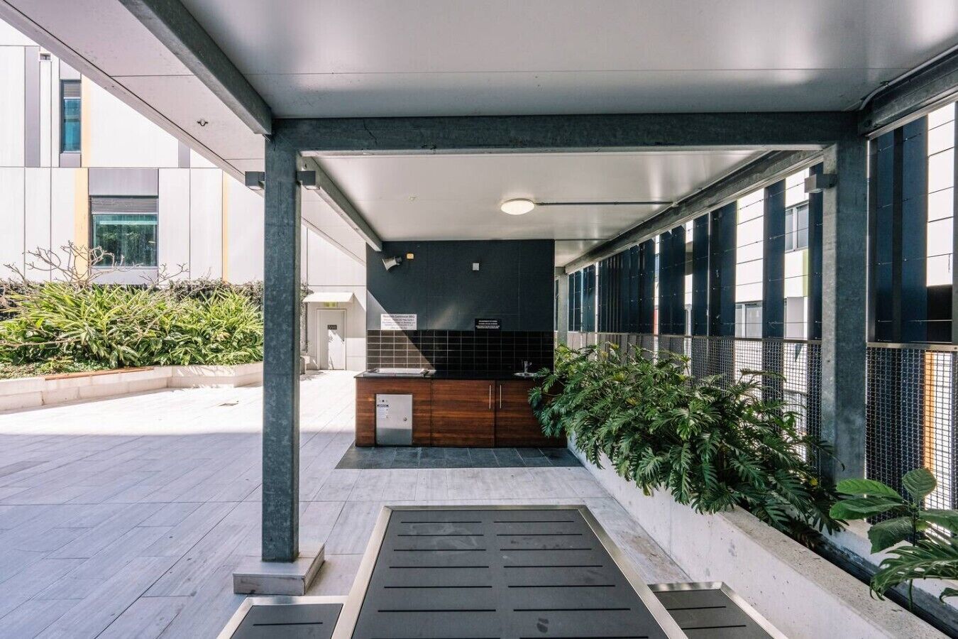 A covered outdoor area with a reception desk, a planter with greenery, and a tiled floor.