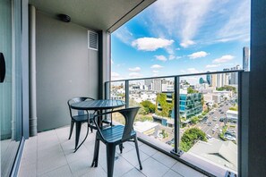 A balcony with a table and chairs, overlooking a cityscape with buildings and a clear sky. - One Bedroom Urban Solace Near CBD (Fortitude Valley)