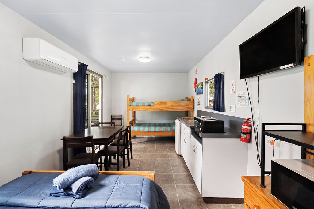 A compact room with a bunk bed, a desk, a chair, a television, and a kitchenette.