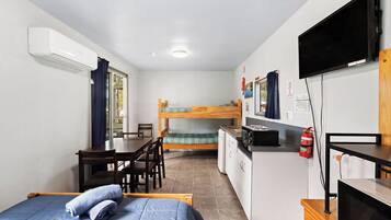 A compact room with a bunk bed, a desk, a chair, a television, and a kitchenette.