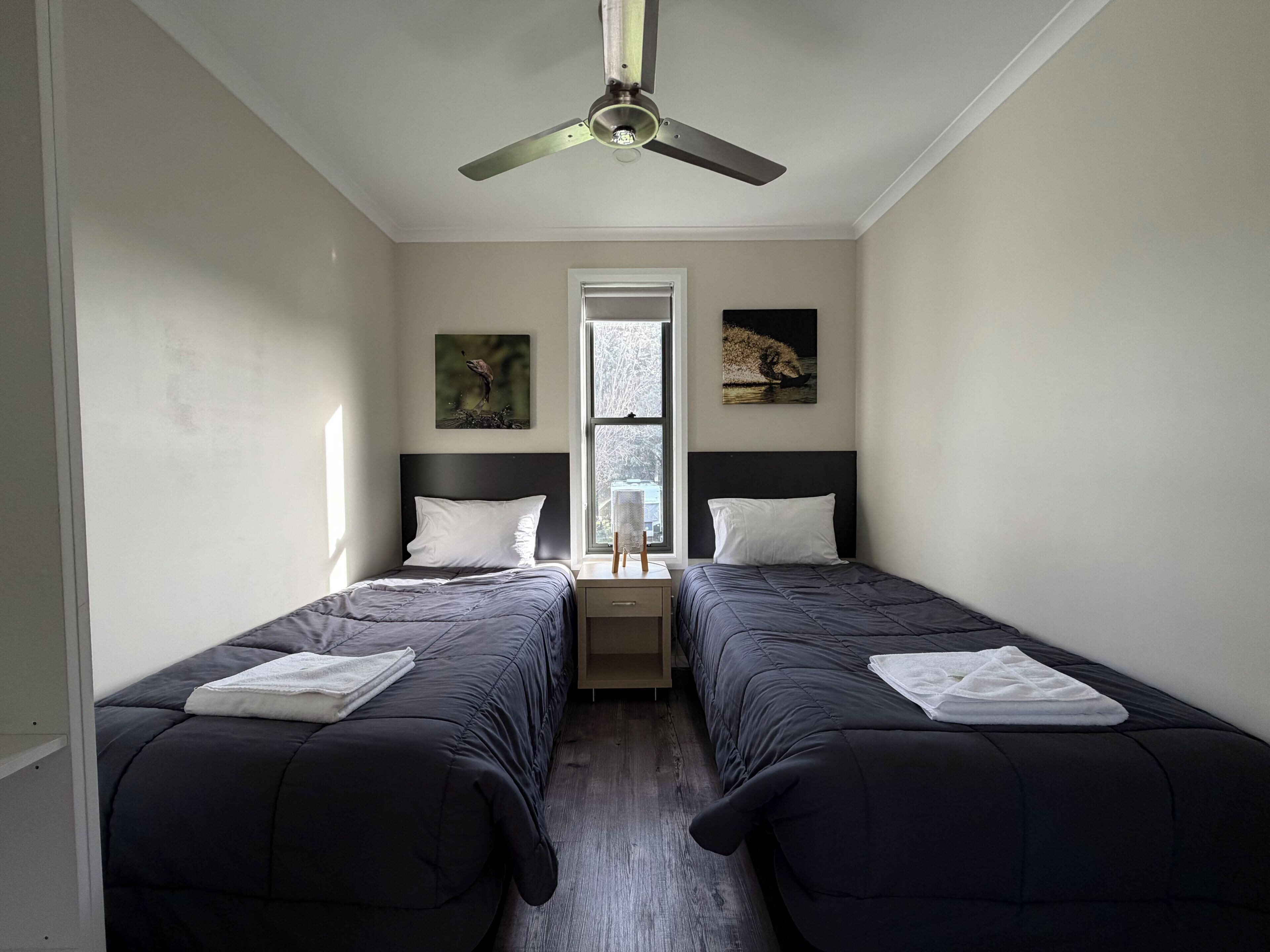 Une chambre avec deux lits, un ventilateur de plafond, une fenêtre et des œuvres d’art accrochées aux murs.
