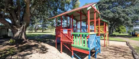 A playground with a red and green play structure, surrounded by trees and a clear sky.