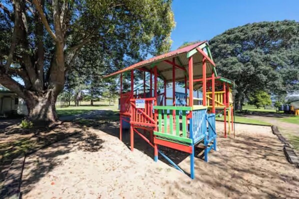 A playground with a red and green play structure, surrounded by trees and a clear sky.