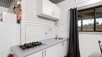 Cocina compacta con estufa a gas, pileta y muebles blancos.