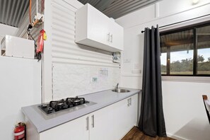 Cocina compacta con estufa a gas, pileta y muebles blancos.