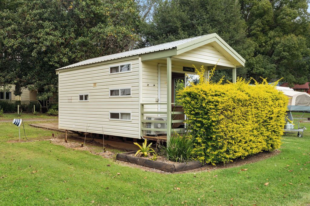 A single-story, light-colored mobile home with a porch and a small garden area with yellow flowering bushes.