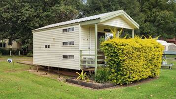 A single-story, light-colored mobile home with a porch and a small garden area with yellow flowering bushes.