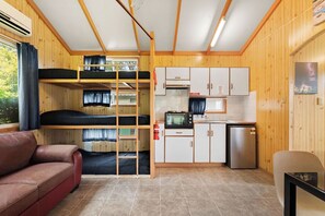 Una habitación pequeña con literas, kitchenette, sofá y una mesita.