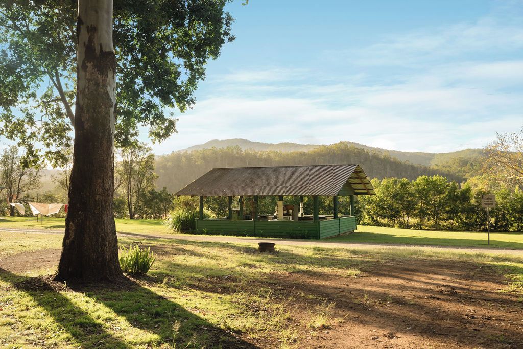 A pavilion with a roof and walls, surrounded by grass and trees, with a mountain in the background.