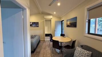 A compact room with a bed, a dining table with chairs, a ceiling fan, and a window with a view.