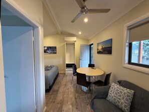 Una habitación compacta con cama, una mesa de comedor con sillas, un ventilador de techo y una ventana con vistas.