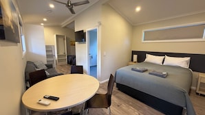 Ein Hotelzimmer mit einem Bett, einem Schreibtisch mit Stühlen, einem Deckenventilator und Blick auf den Flur.