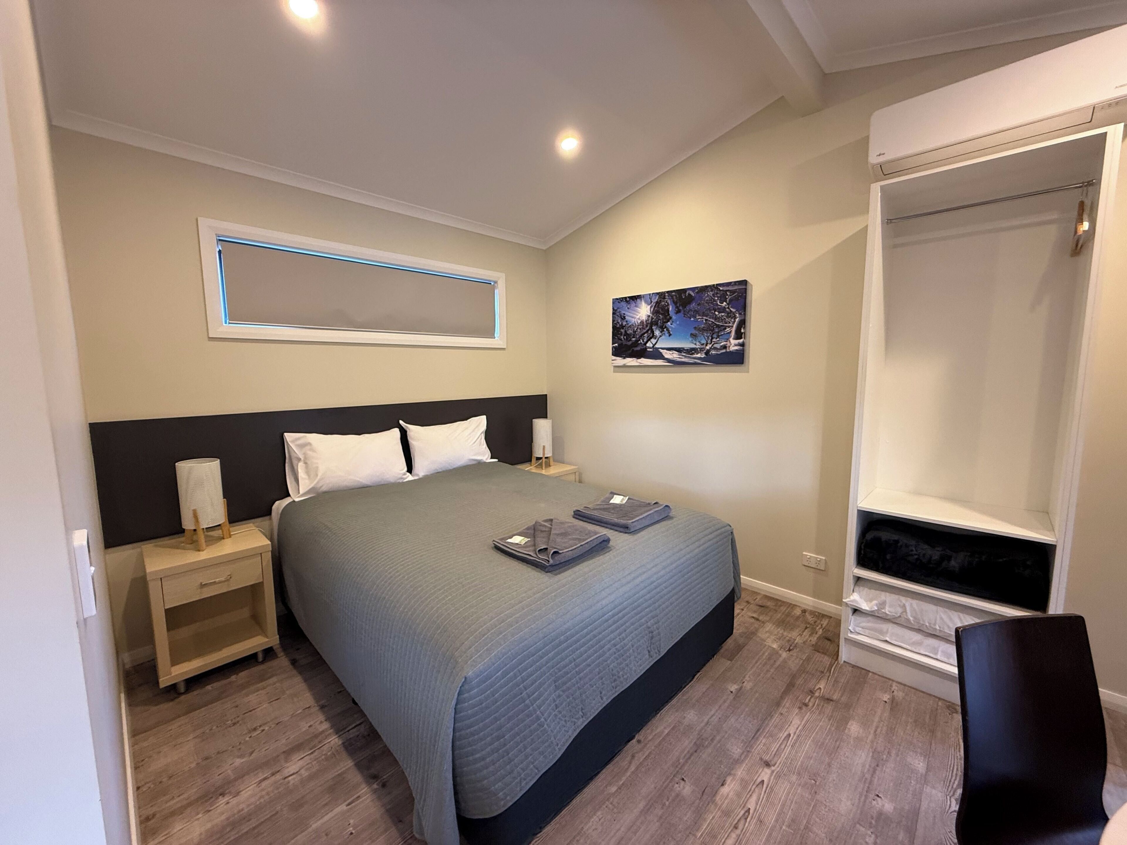 Un dormitorio con cama, mesitas de noche, una ventana con vistas y una obra de arte en la pared.