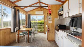 A compact kitchen with a dining area, wooden walls, and a view through a glass door.