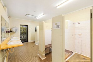 A public restroom with multiple sinks, a shower area, and a sign indicating a 5-minute maximum shower time.