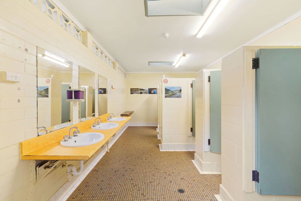 Un baño alargado y estrecho con varios lavamanos y espejos, paredes con azulejos y piso estampado.