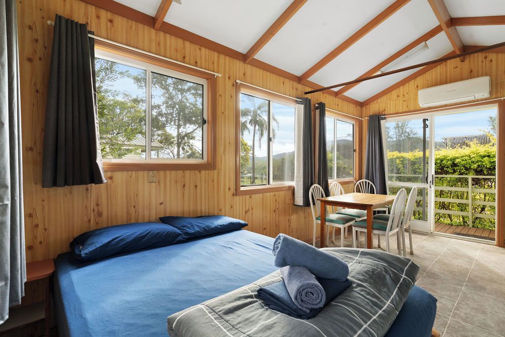 A room with a bed, a table with chairs, and large windows.