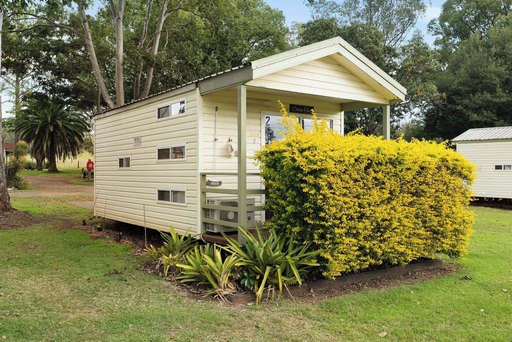 A single-story mobile home with a porch, surrounded by a well-maintained lawn and a bush with yellow flowers.