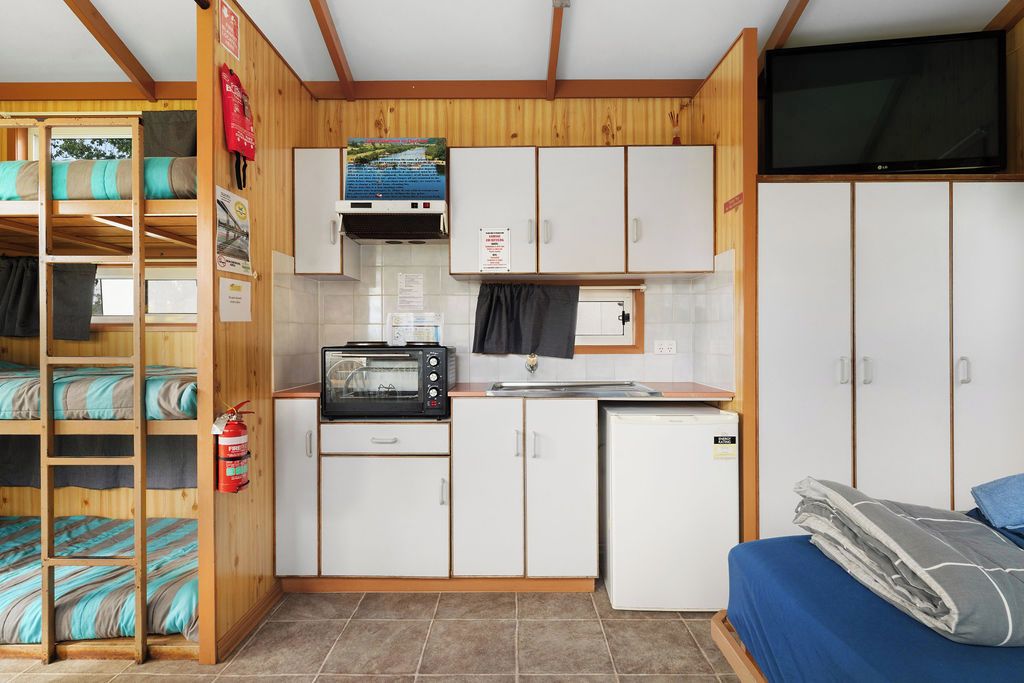A compact kitchenette with a microwave, toaster, and small refrigerator. There is a bunk bed with blue bedding and a television mounted on the wall.