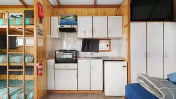 A compact kitchenette with a microwave, toaster, and small refrigerator. There is a bunk bed with blue bedding and a television mounted on the wall.
