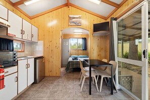 A compact kitchen with a microwave, stove, and sink, a dining area with a table and chairs, and a bedroom with a bed and window.