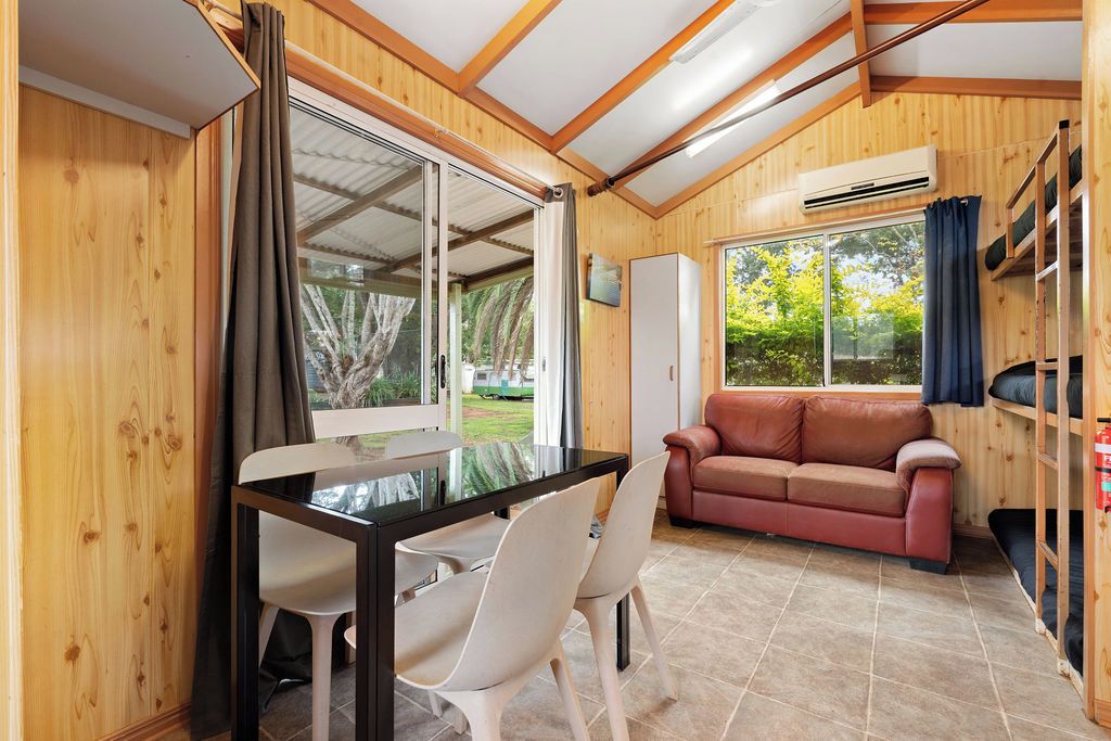 A room with a wooden interior, a glass table with chairs, a sofa, and a window with curtains.