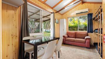 A room with a wooden interior, a glass table with chairs, a sofa, and a window with curtains.