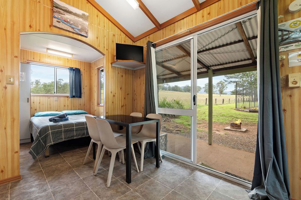 A room with a bed, a table with chairs, a TV mounted on the wall, and a sliding glass door leading to an outdoor area.