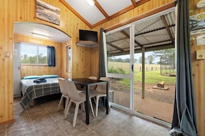 A room with a bed, a table with chairs, a TV mounted on the wall, and a sliding glass door leading to an outdoor area.