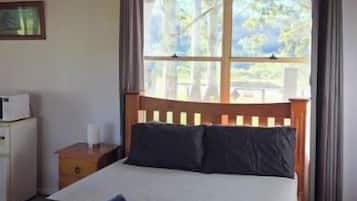 A bedroom with a bed, a ceiling fan, a window with curtains, a bedside table, and a nightstand.