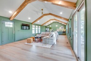 A spacious living area with a high ceiling and exposed wooden beams, a kitchen with green cabinets, and a large window providing natural light. - Lakeside 2BR Cabin Table Rock Lake - Sunset Views (Eagle Rock)