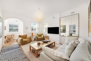 A modern living room with a sofa, armchairs, a coffee table, and a TV. - Casa Franka - Art Deco Beachfront Apartment in North Bondi (Bondi Beach)