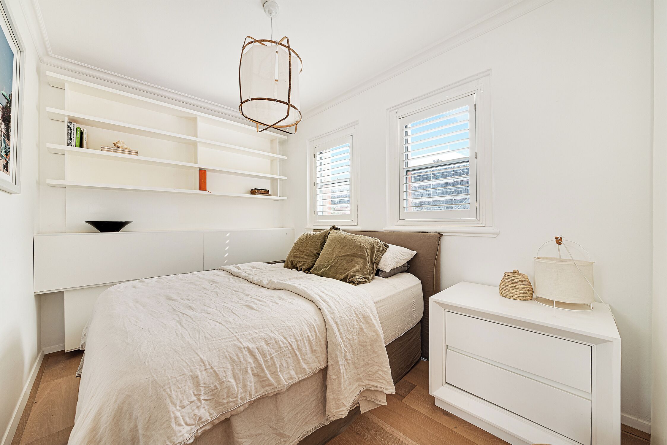 A bedroom with a bed, bedside table, shelves, and a window.