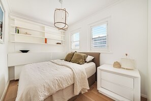 Une chambre à coucher avec un lit, une table de chevet, des étagères et une fenêtre.
