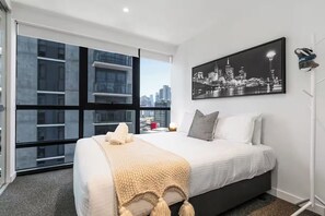 Et moderne hotelværelse med en stor seng, udsigt over bybilledet og et billede i ramme på væggen.