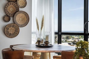 A dining area with a round table, brown chairs, and decorative woven plates on the wall. - Skyline & Bay Views Stylish 3BR Southbank Retreat (Southbank)