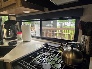 A kitchen with a gas stove, kettle, coffee maker, and a window overlooking a deck. - Suite Escape on the Lake (Nevis)