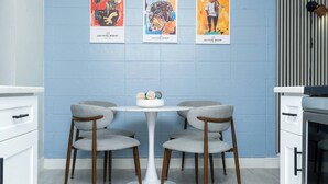 Eine moderne Küche mit einem runden Tisch, vier grauen Stühlen und drei farbenfrohen Bildern an der Wand.