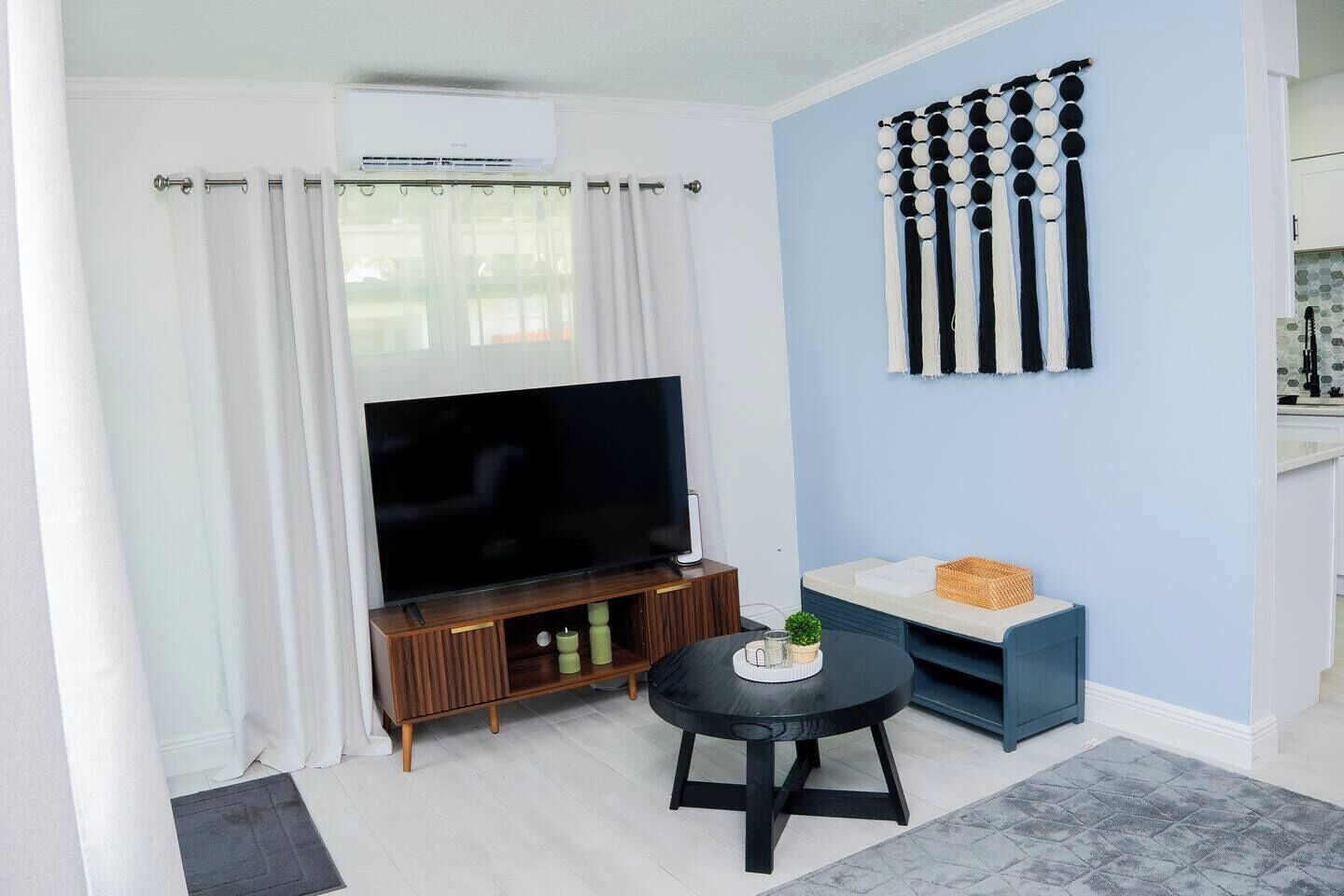 Una sala de estar con televisor de pantalla plana, una mesita redonda y un sofá azul.