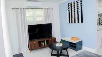 Una sala de estar con televisor de pantalla plana, una mesita redonda y un sofá azul.