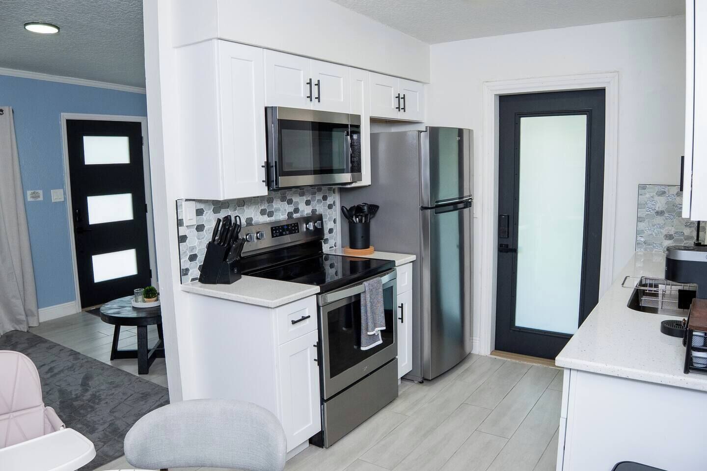 A compact kitchen with white cabinets, a microwave, a stainless steel refrigerator, and a small dining area with a table and chairs.