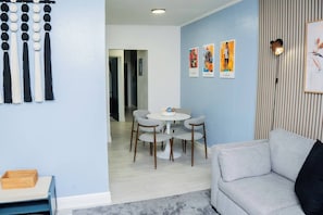 A modern living room with a grey sofa, a round dining table with chairs, and a wall with vertical wooden slats and framed artwork. - City Life Meets Quiet Comfort (Orlando)