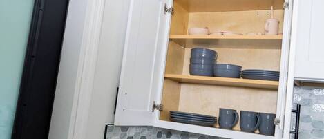 Una cocina con un armario que contiene platos, tazones y tazas.