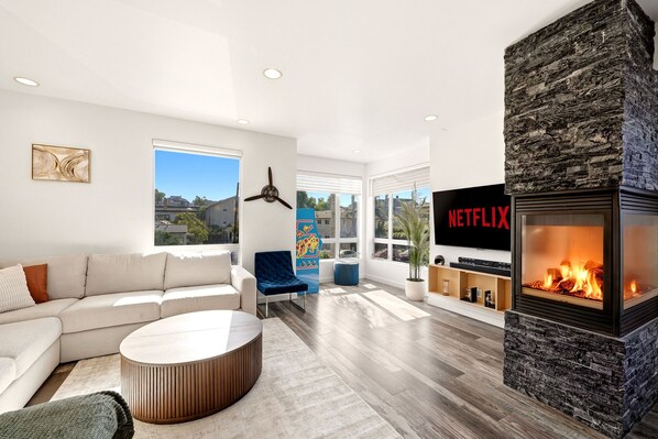 Un salon moderne avec une cheminée, un canapé, une table basse et un téléviseur affichant le logo de Netflix.
